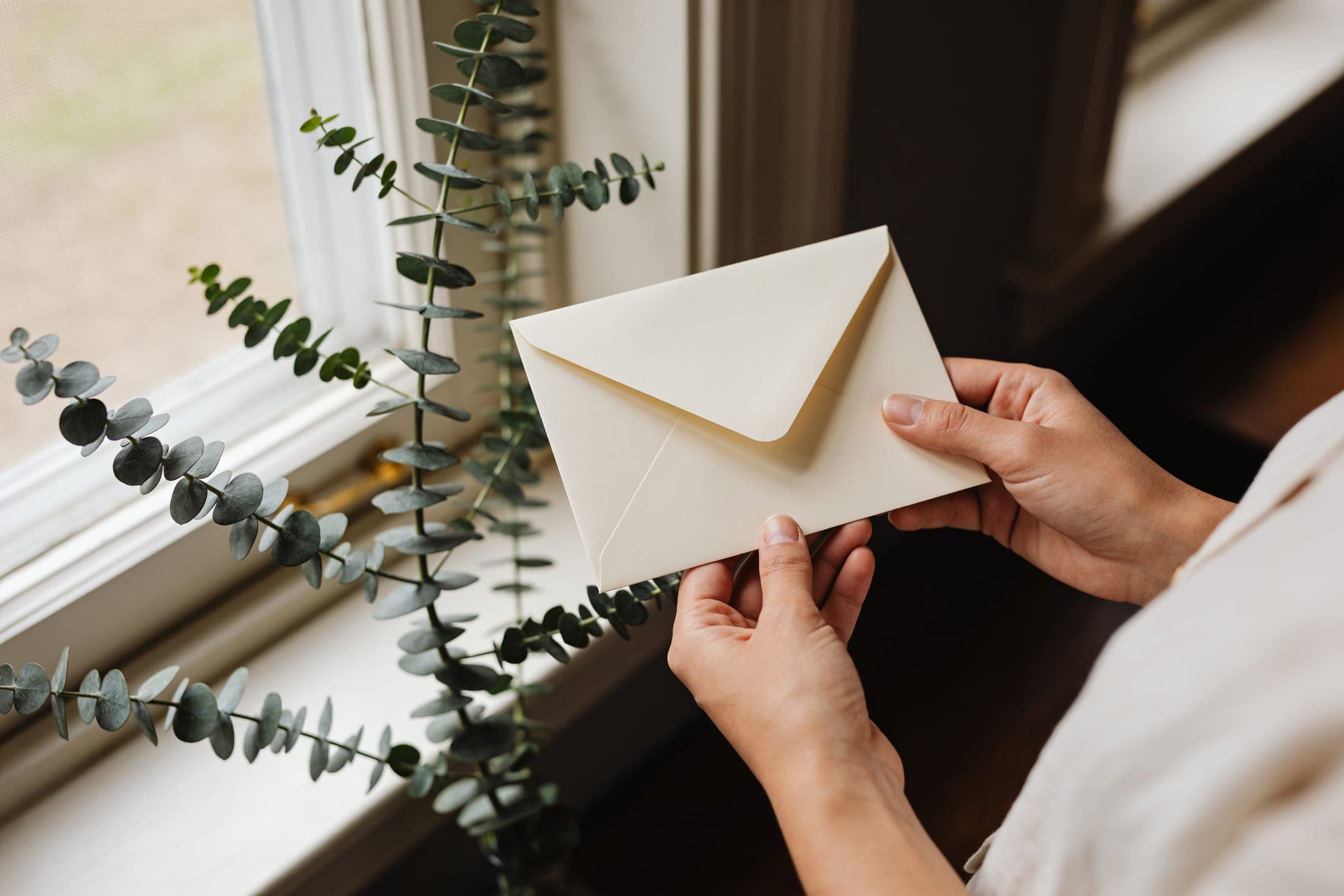 A sealed envelope held gently near a sunlit window.