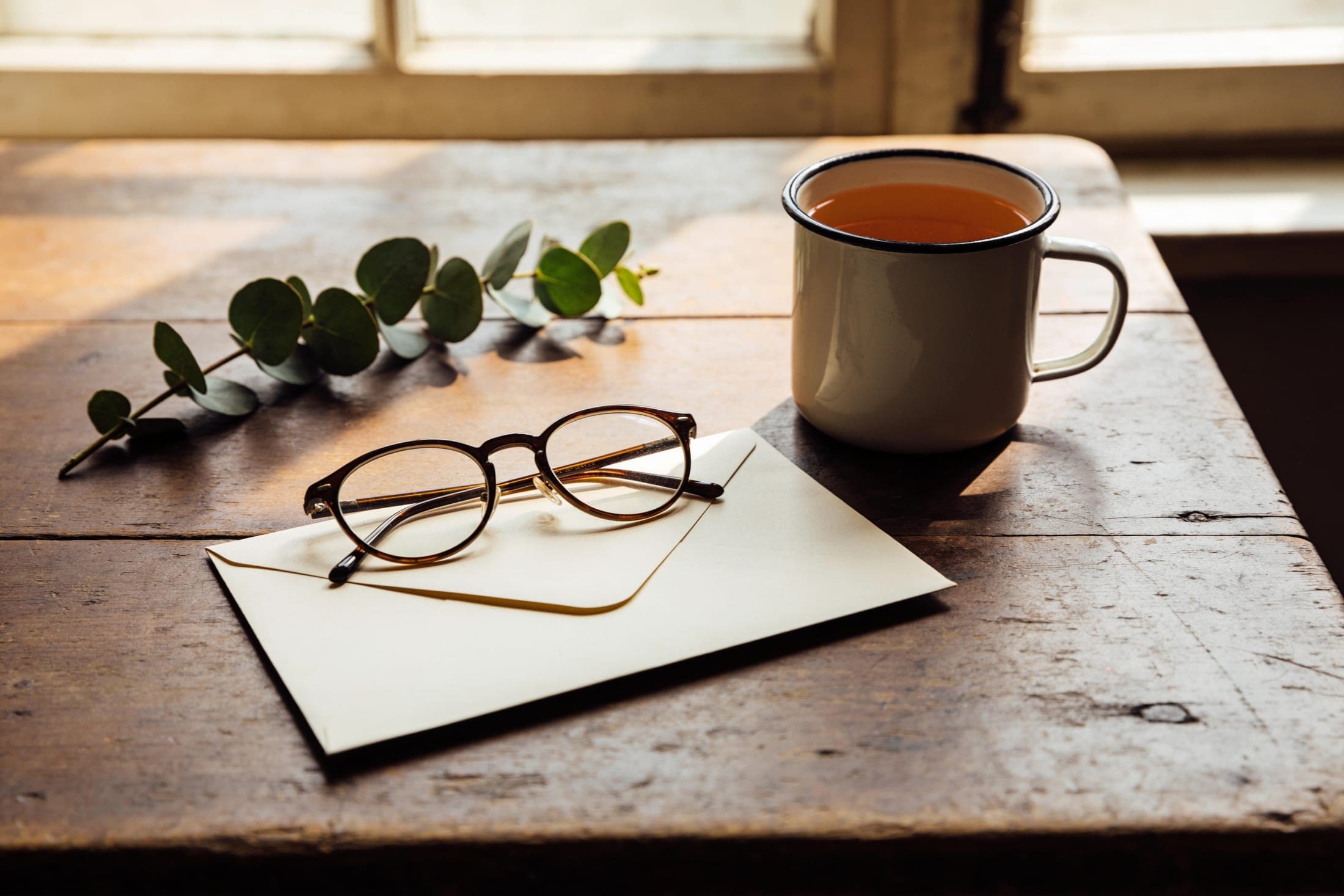 Reading glasses resting on a folded letter beside a cup of tea.